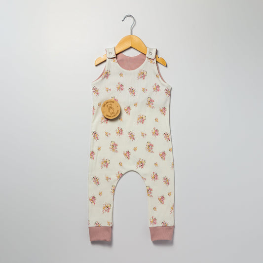 Floral patterned baby and children’s romper with pink accents on a hanger against a white background